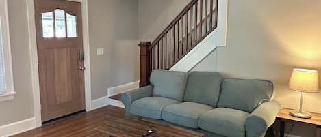 A living room with a wooden floor, a light blue sofa, a wooden coffee table, a lamp, and a staircase.