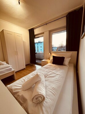 Hotellihuone, jossa on sänky, vaatekaappi, yöpöytä ja ikkuna, josta on näkymä rakennuksiin.