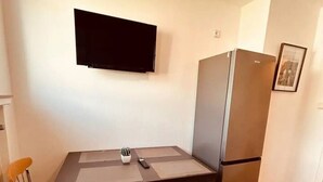 Cocina compacta con mesa, sillas, televisor de pantalla plana y refrigerador.