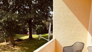 Un balcón con una silla, una mesita pequeña, un árbol y una zona ajardinada.