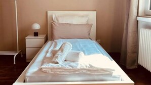 Un lit bien fait, agrémenté d’oreillers et de serviettes, une table de chevet avec une lampe, et une œuvre d’art florale encadrée accrochée au mur.