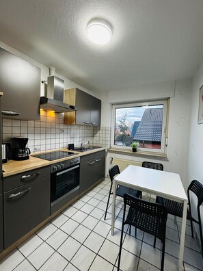 Een moderne keuken met een eethoek, met een raam met uitzicht op huizen, een ingebouwde oven en een koffiezetapparaat.