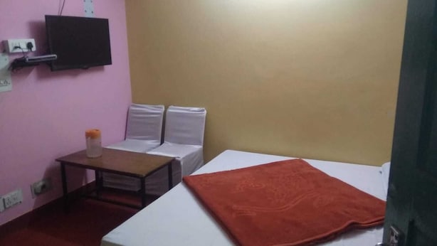A small, pink and beige room with a bed, a table, and a TV mounted on the wall. - Hotel Grand Kailash (Joshimath)