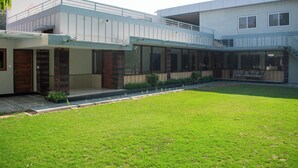 A modern two-story house with a covered patio, a well-maintained lawn, and a staircase leading to an upper level. - Villa Vilas (Udaipur)