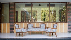 A seating area with three chairs and a sofa in front of a large window with a view of a building and trees. - Villa Vilas (Udaipur)
