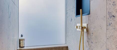A shower with a glass door, a handheld showerhead, and a small bottle of shampoo on the ledge.