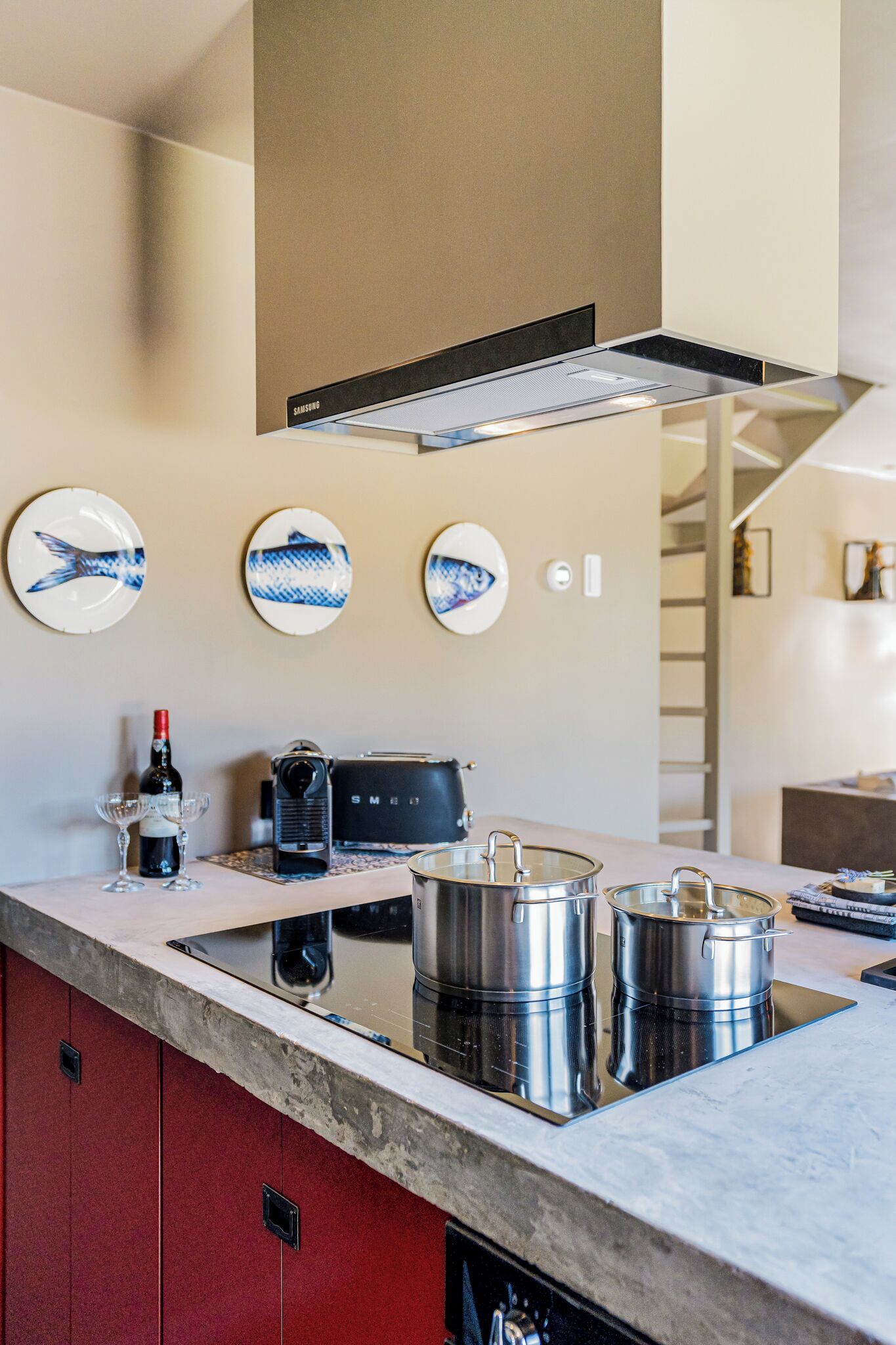 A modern kitchen with a built-in stove, stainless steel pots, and a coffee maker. There are decorative plates on the wall and a wine bottle on the counter.