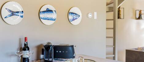 A modern kitchen with a built-in stove, stainless steel pots, and a coffee maker. There are decorative plates on the wall and a wine bottle on the counter.