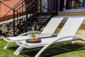 Two white lounge chairs with a small table between them, a glass of water, and a bottle of champagne.