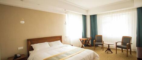 A hotel room with a large bed, two armchairs, a small table, and a desk.