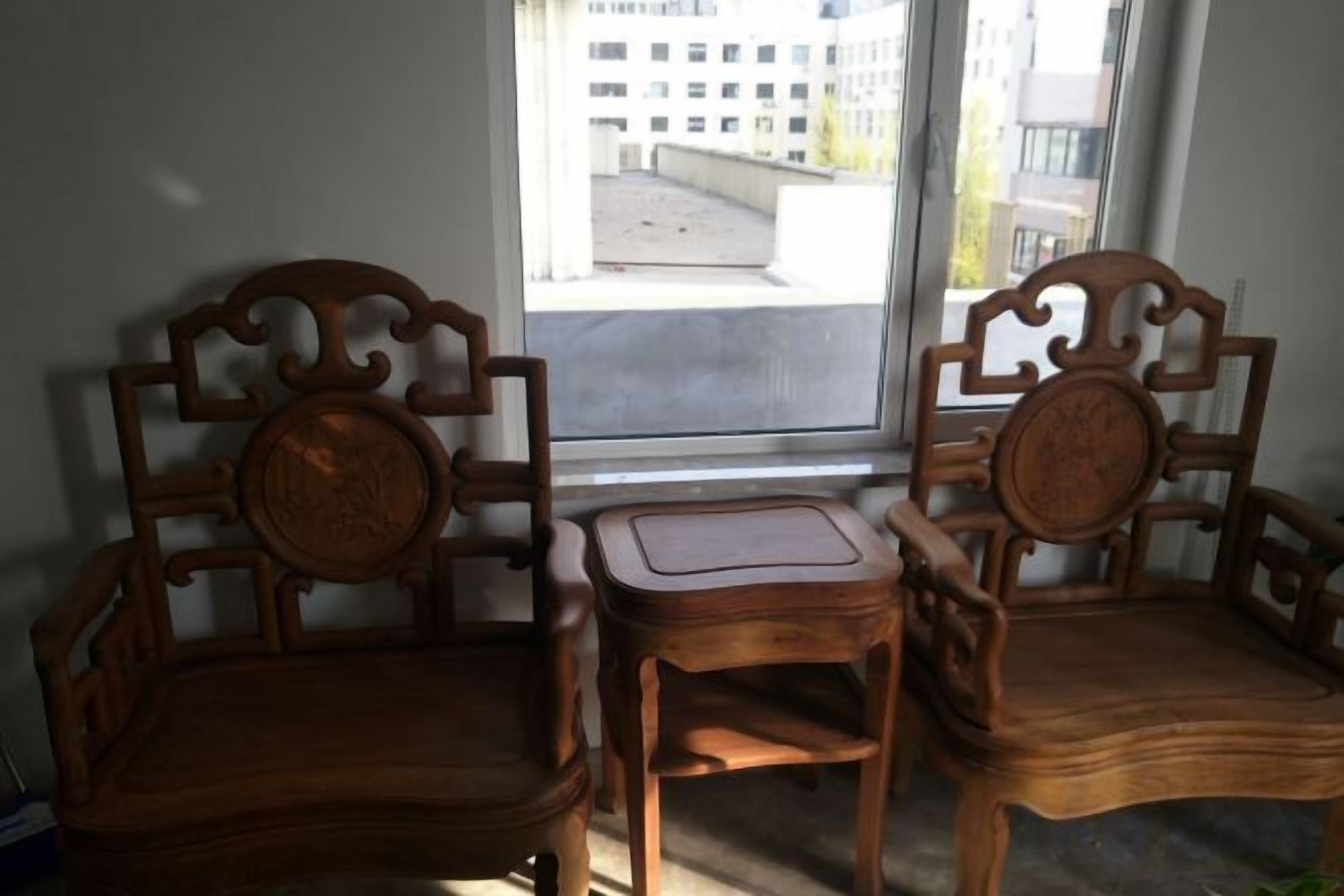 Dos sillas de madera y una mesita en una habitación con ventana.