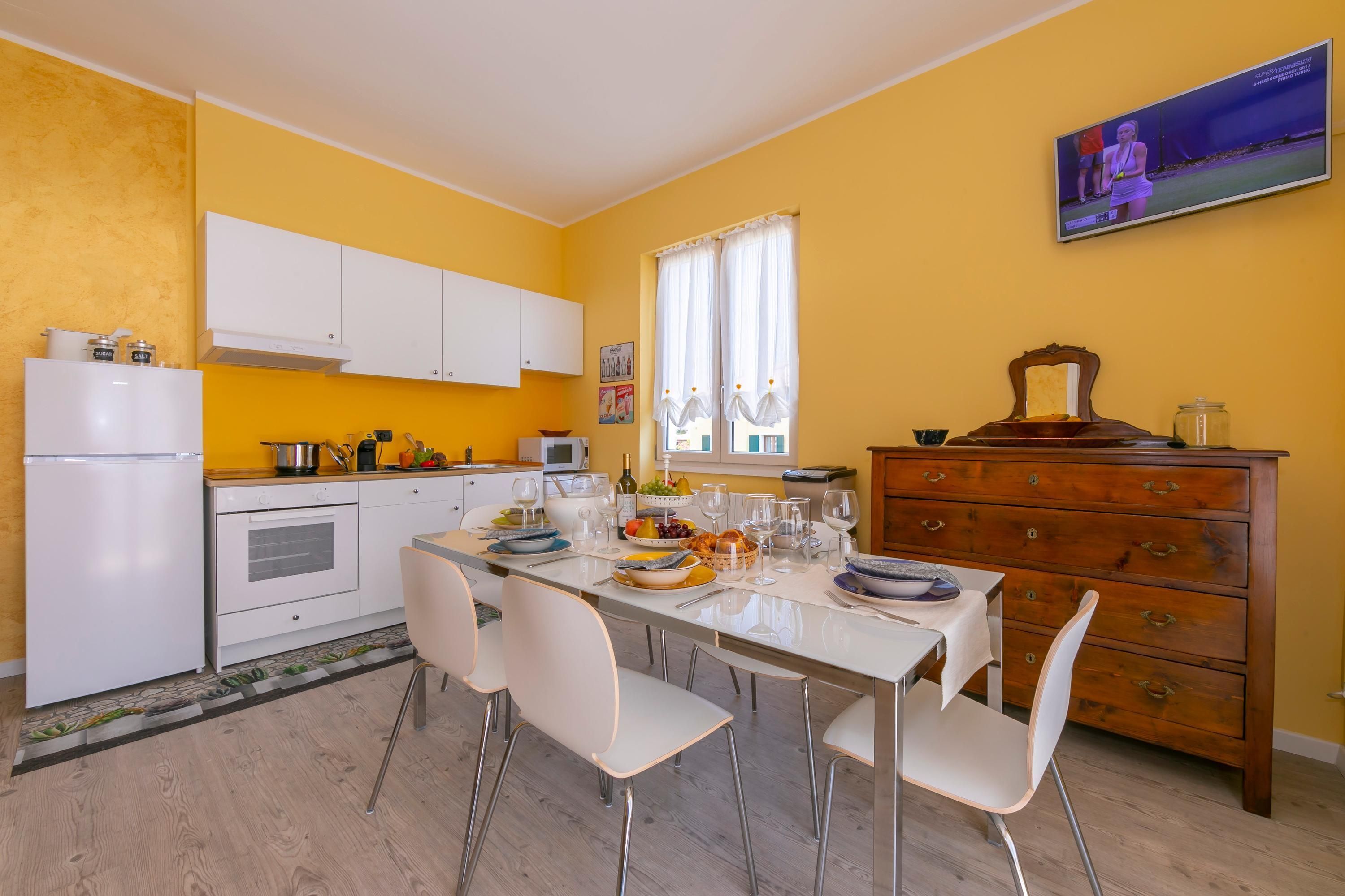 Une cuisine compacte avec des meubles blancs, une table à manger pour quatre personnes et une commode en bois dotée de tiroirs.