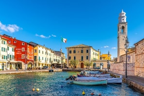 A waterfront scene with colorful buildings, a bell tower, and boats docked along the water. - Casa Mondragon In Lazise (Lazise)
