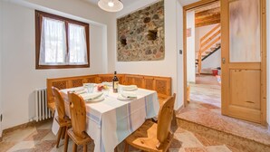 A dining area with a table set for four, a stone wall, a window with curtains, and a wooden door leading to a staircase.