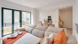 A modern hotel room with a large bed, a kitchenette, and a balcony with a view.