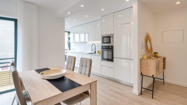 A modern kitchen with white cabinets, a wooden dining table, and a small wooden side table with decorative items.