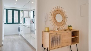 A modern kitchen with white cabinets, a wooden cabinet with a sunburst mirror, and a washing machine.