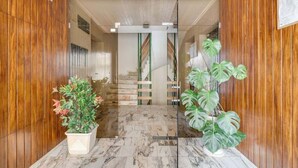 A wooden-paneled hallway with marble flooring, leading to a staircase. There are two potted plants on either side.