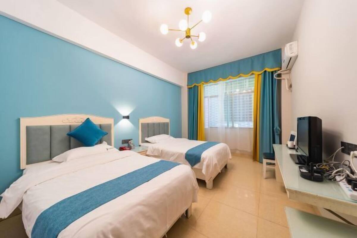 A hotel room with two beds, a desk with a computer, a TV, and an air conditioning unit.