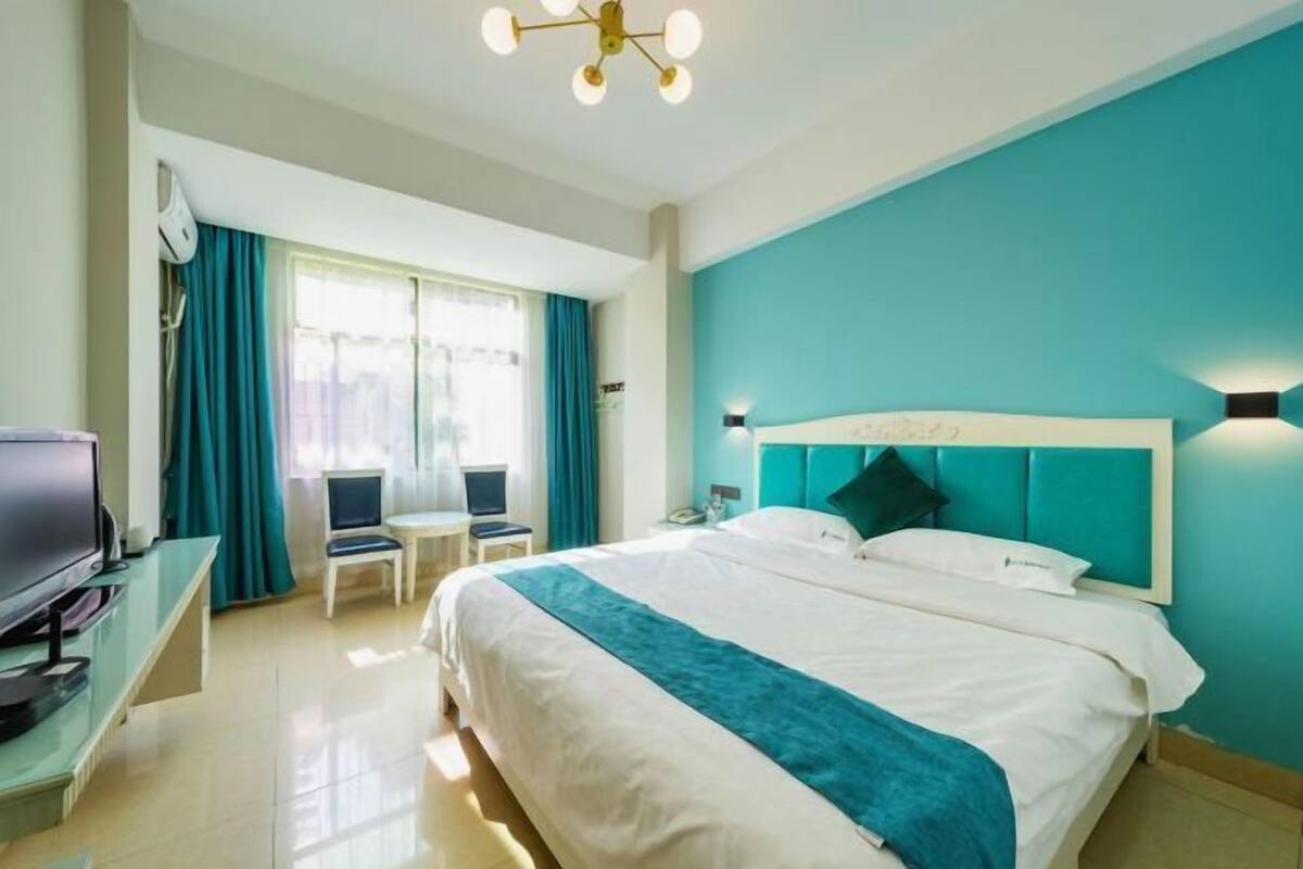 A hotel room with a bed, a desk with a computer, a television, and a window with curtains.