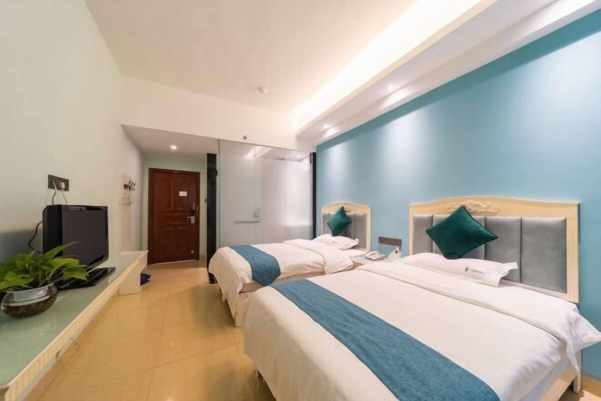 A hotel room with two beds, a TV, a plant, and a door leading to another room.