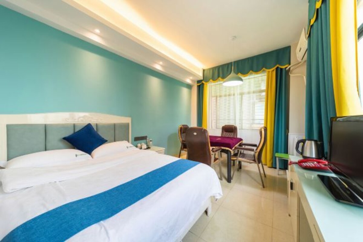 A hotel room with a bed, a desk with a computer, a chair, a table, and curtains.