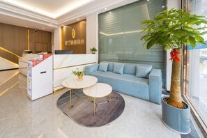 A reception area with a reception desk, a sofa, two tables, and a potted plant. - Tinglan Light Stay Hotel (Haikou)