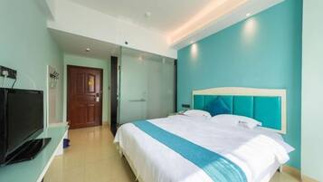 A modern hotel room with a large bed, a television on a stand, and a door leading to another room.