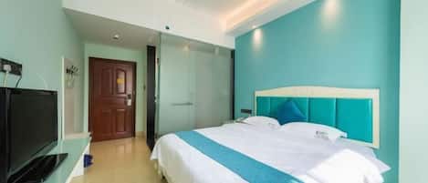 Una habitación de hotel moderna con una cama grande, un televisor sobre un mueble bajo y una puerta que da a otra habitación.