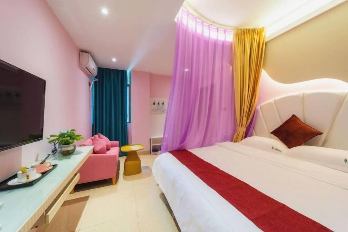 A modern hotel room with a bed, a desk, a TV, and a plant.