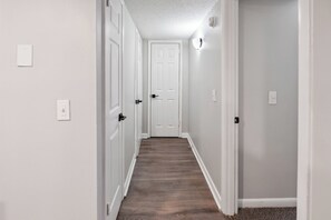 A narrow hallway with a wooden floor, white walls, and a white door at the end. - Brentwood A2 I Cozy & Comfy I 2Bd I Free Parking (Nashville)