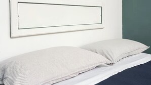 A bed with a white mattress and striped pillows, a white headboard, and a small shelf with a mirror and light fixture above it. - [Cactus-Room] (Padova)