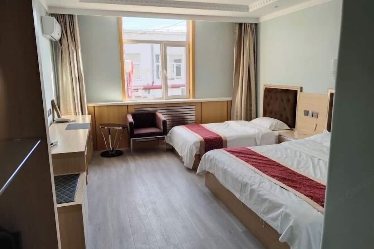 Hotellihuone, jossa on kaksi sänkyä, työpöytä, tuoli ja ikkuna, jossa on verhot.
