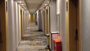 Un couloir d’hôtel avec un tapis à motifs, des portes de chaque côté et un buffet rouge.