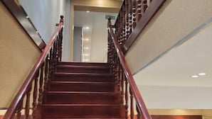 Un escalier en bois, doté d’une rampe, mène à un espace intérieur où est fixée une enseigne au mur.