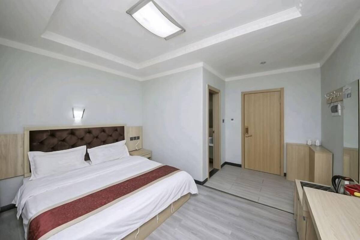 Hotellihuone, jossa on sänky, yöpöytä, yölamppu ja ovi, joka johtaa toiseen huoneeseen.