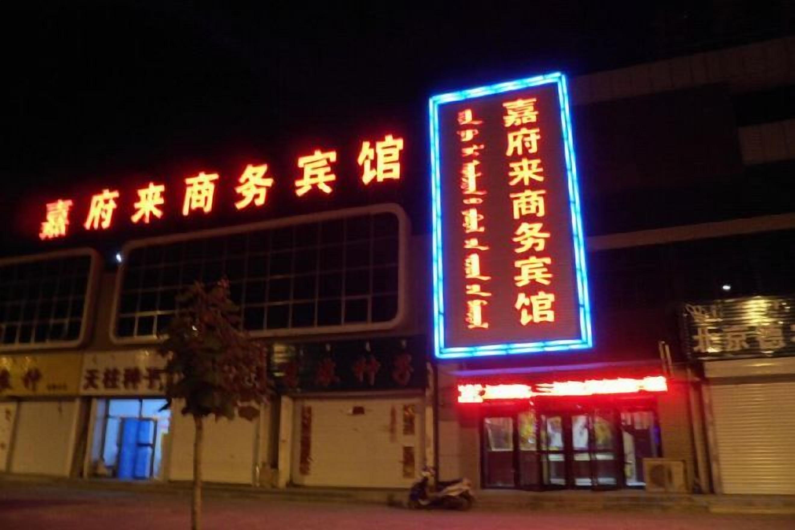 A building with a large illuminated sign in Chinese characters, a storefront with a red awning, and a tree in front.