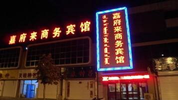 A building with a large illuminated sign in Chinese characters, a storefront with a red awning, and a tree in front.