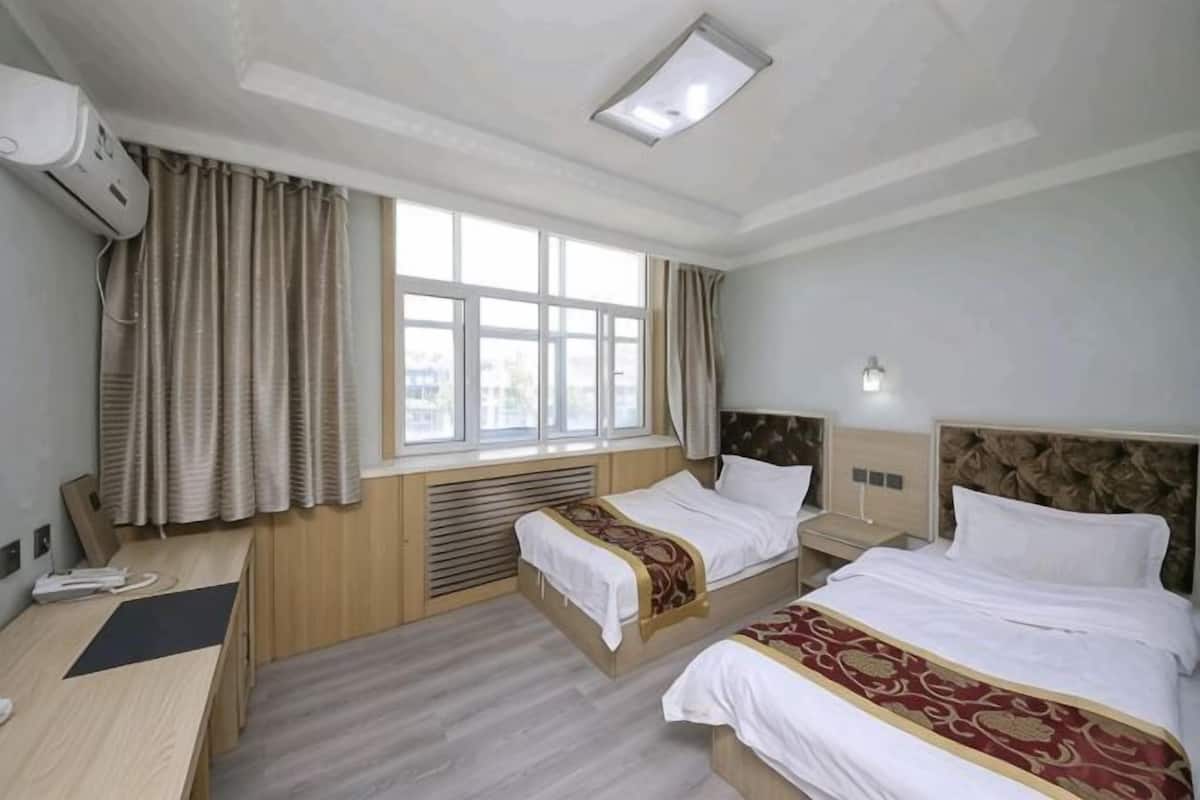 Hotellihuone, jossa on kaksi sänkyä, työpöytä, tuoli, ikkuna ja kattovalaisin.
