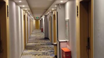 A hotel corridor with doors on both sides, a patterned carpet, and a red object on the right.