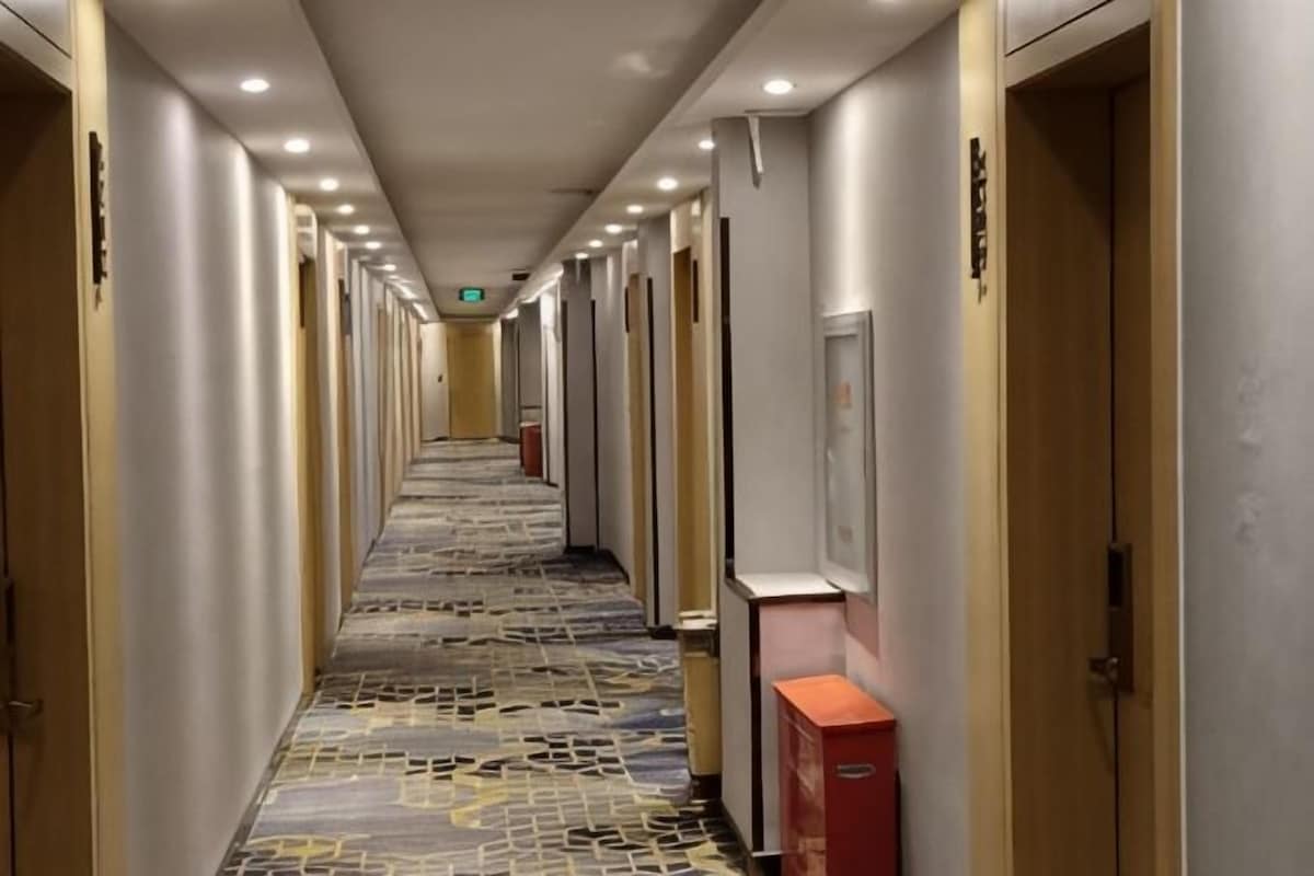 Ein Hotelgang mit Türen an beiden Seiten, einem gemusterten Teppich und einem roten Gegenstand rechts.