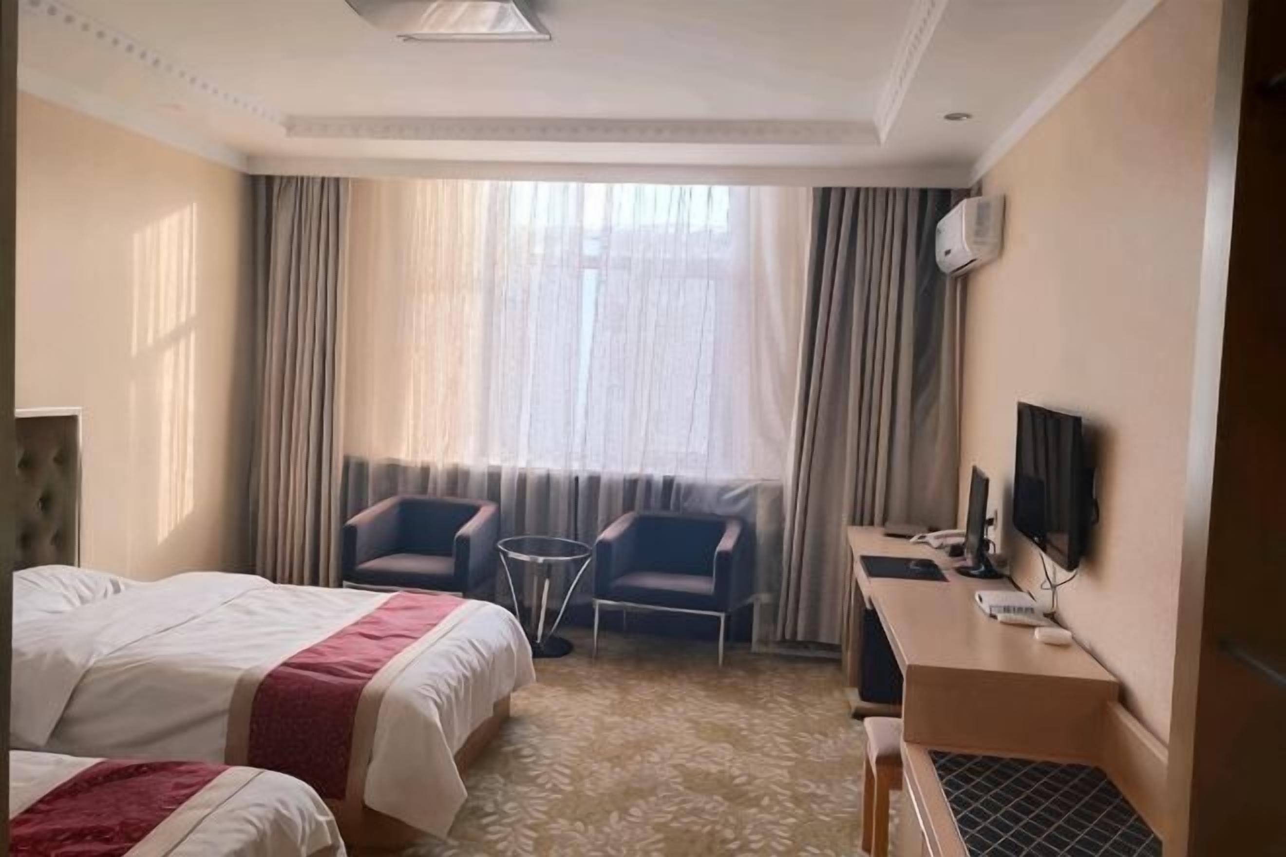 Et hotelværelse med to senge, et skrivebord, en stol, et fjernsyn og et vindue med gardiner.