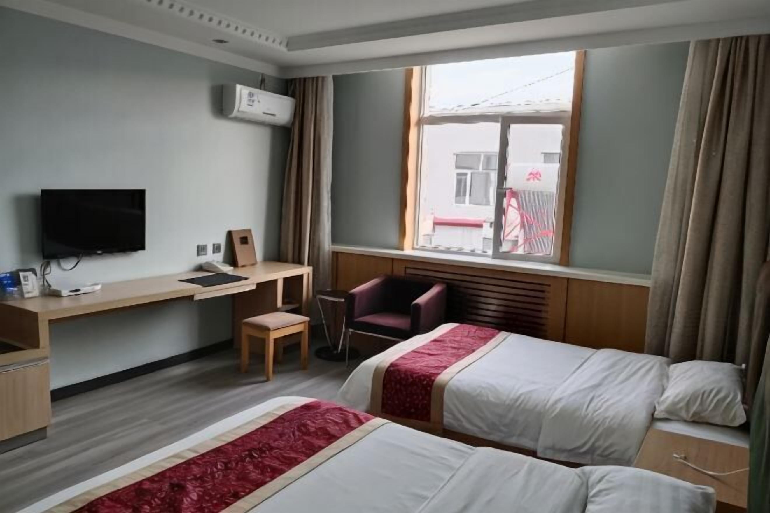 Ein Hotelzimmer mit zwei Betten, einem Schreibtisch mit Stuhl, einem Fernseher und einem Fenster mit Vorhängen.