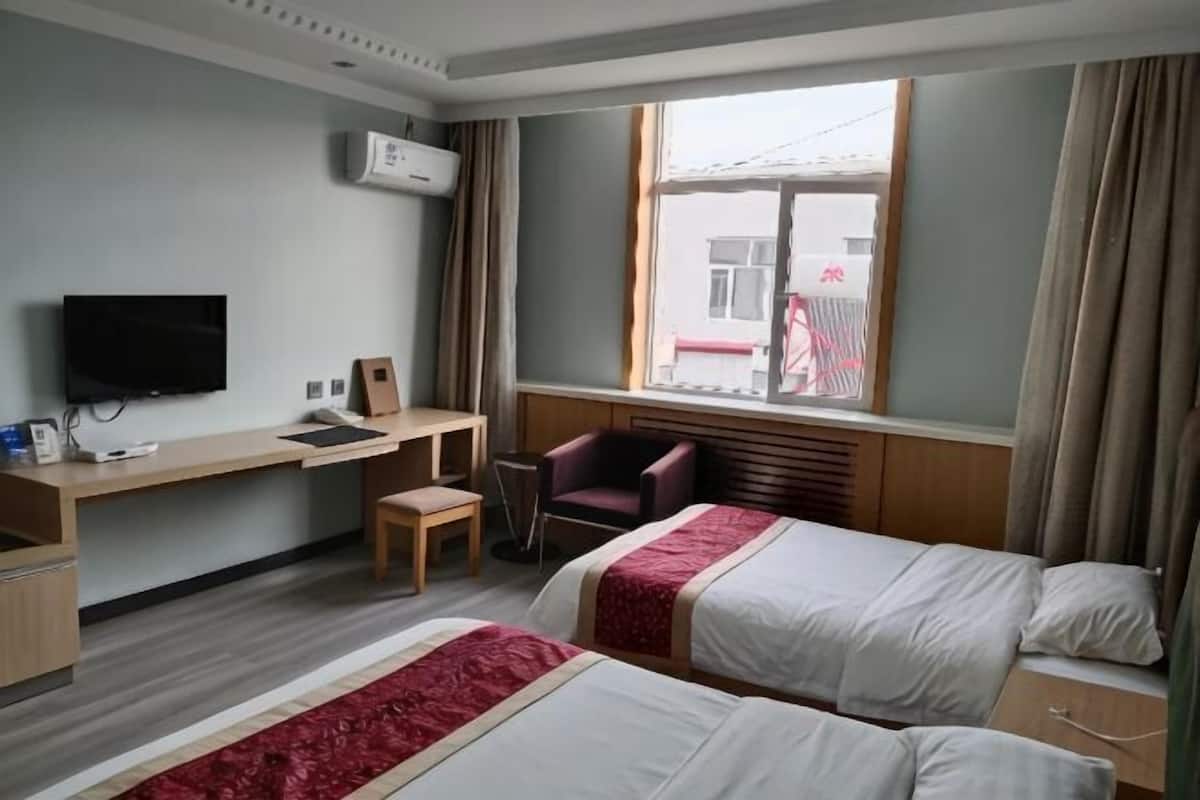 Hotellihuone, jossa on kaksi sänkyä, työpöytä tuolilla, televisio ja ikkuna, jossa on verhot.