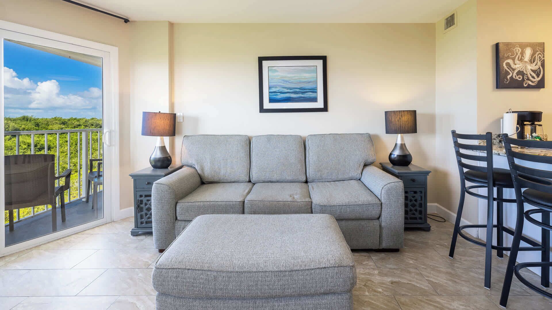 A living room with a grey sofa, two side tables with lamps, a coffee table, and a dining area with a table and chairs.