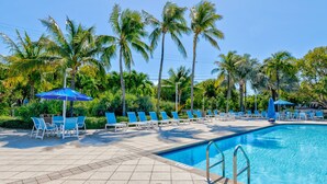 Ein Swimmingpool mit blauen Liegestühlen und Sonnenschirmen, umgeben von Palmen.