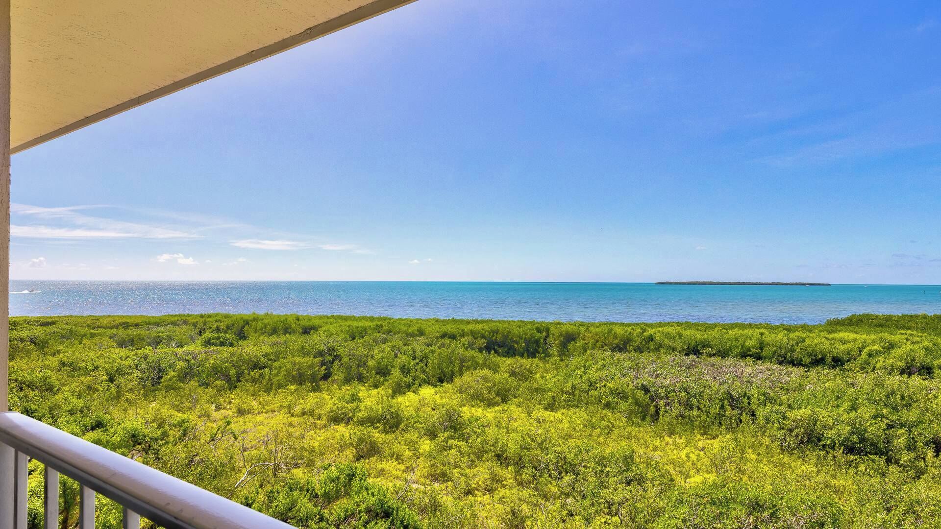 A balcony with a view of a coastal area featuring dense green vegetation and a clear blue sky.