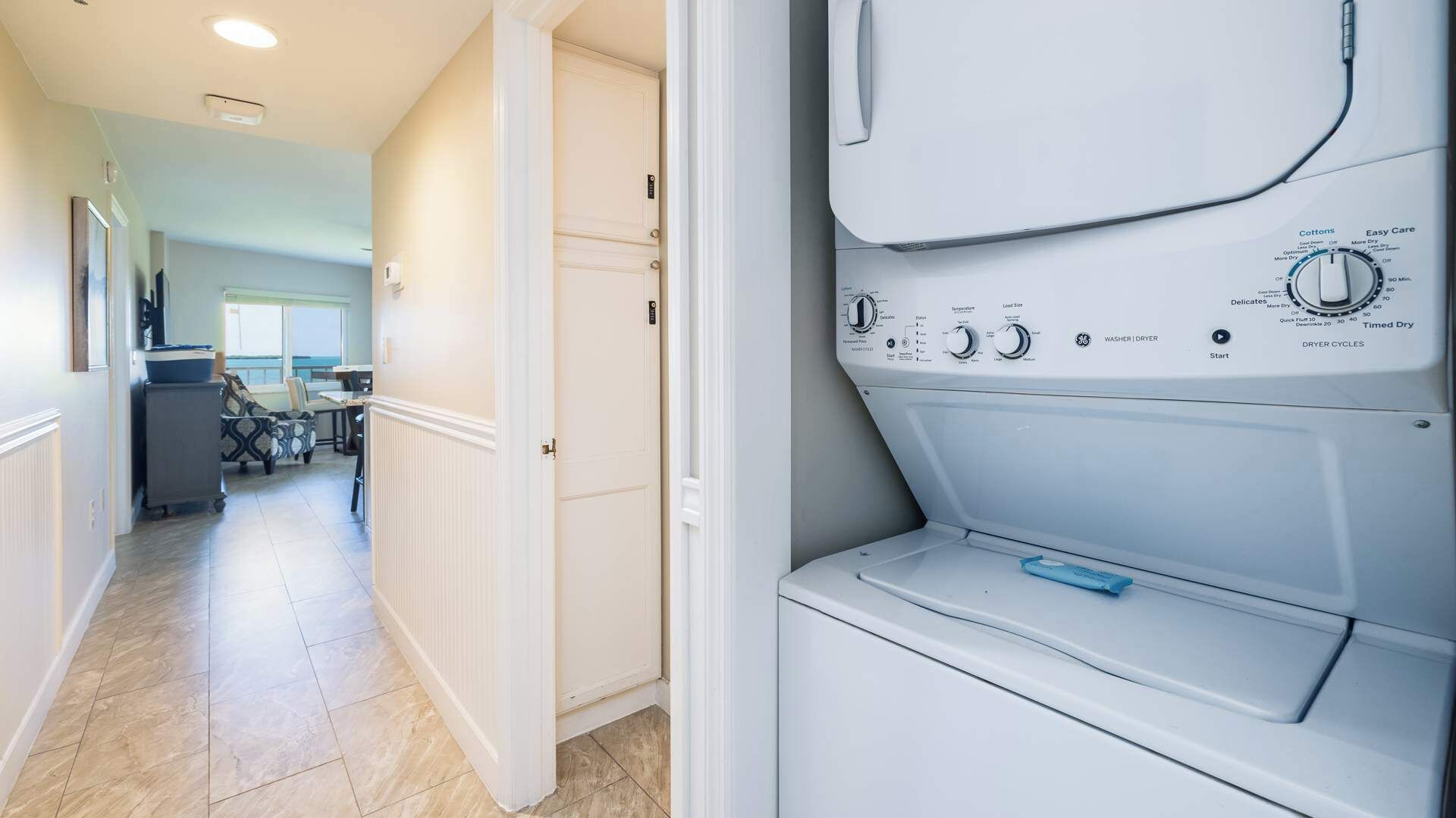 A laundry room with a front-loading washing machine, a dryer, and a door leading to a hallway with a dining area.