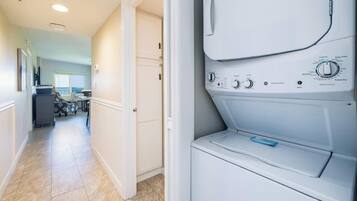 A laundry room with a front-loading washing machine, a dryer, and a door leading to a hallway with a dining area.