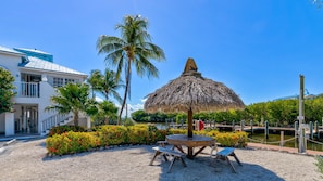 A beachfront property with a thatched umbrella, a wooden table, and benches.